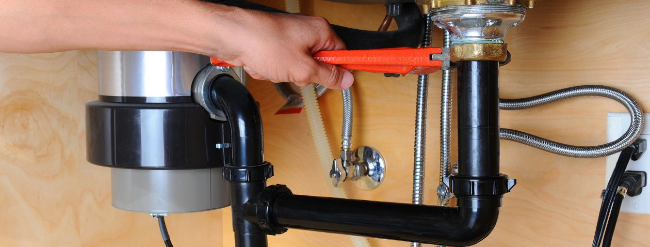 A plumber is working on a garbage disposal. 